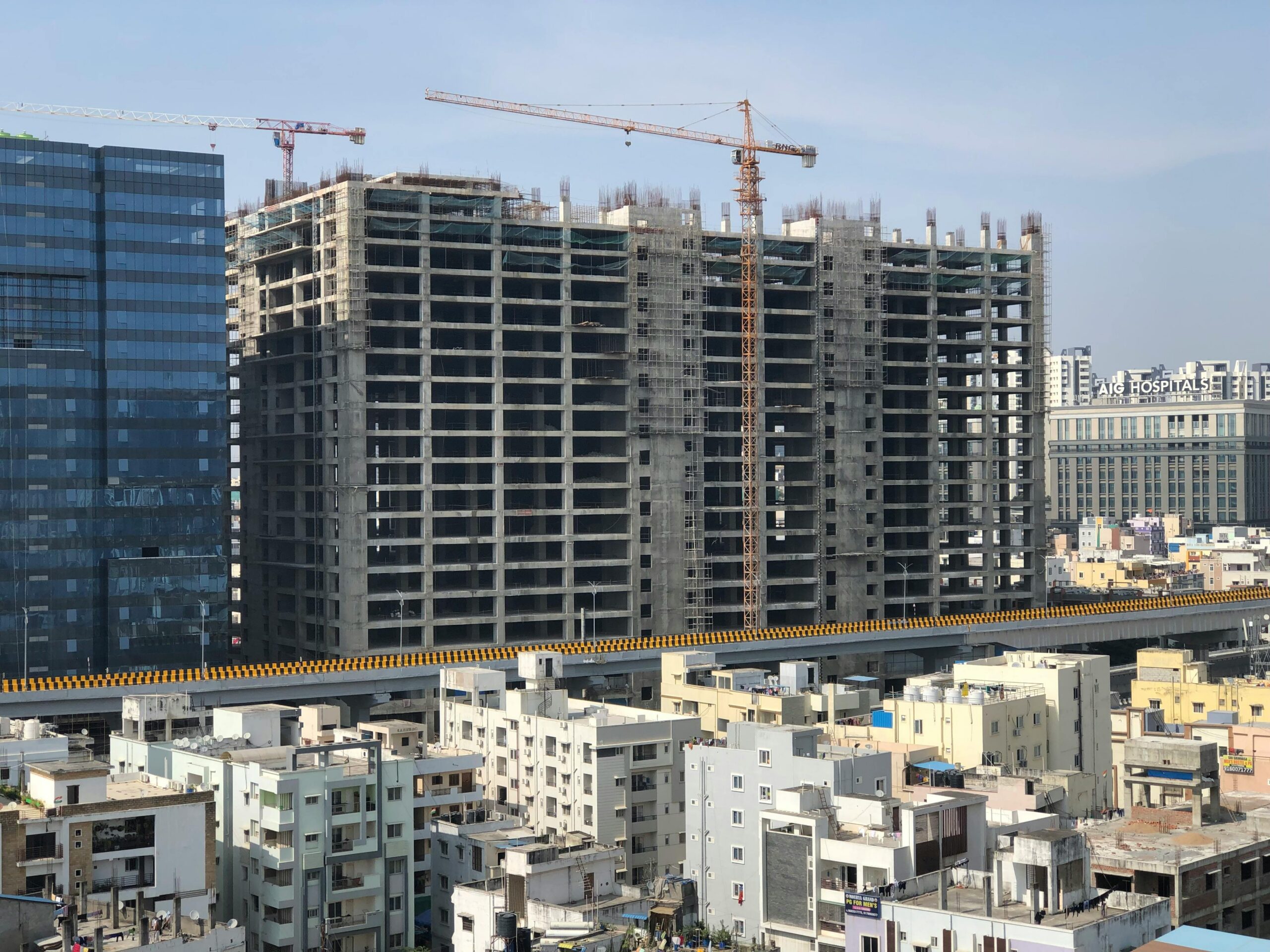 High-rise building under construction in a bustling city with cranes and urban infrastructure.